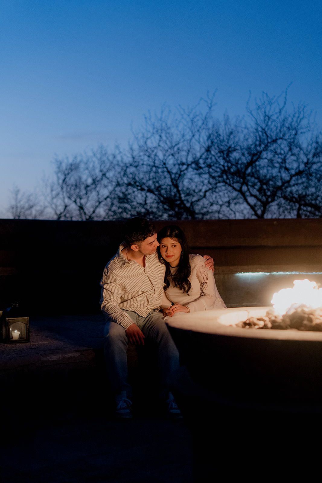 Romantic evening scene with couple sitting by illuminated fire pit outdoors.