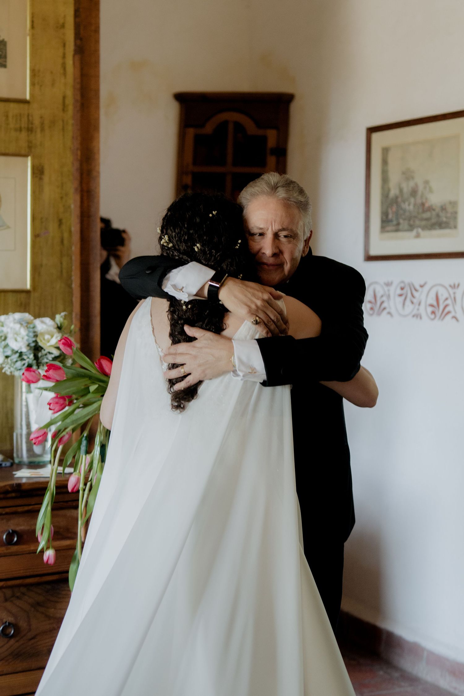 Emotional embrace in a sunlit room with white wedding dress.