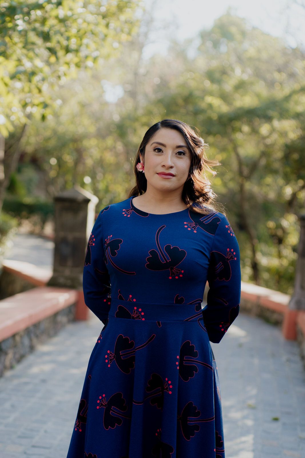 A woman in a navy blue dress with floral details poses outdoors.