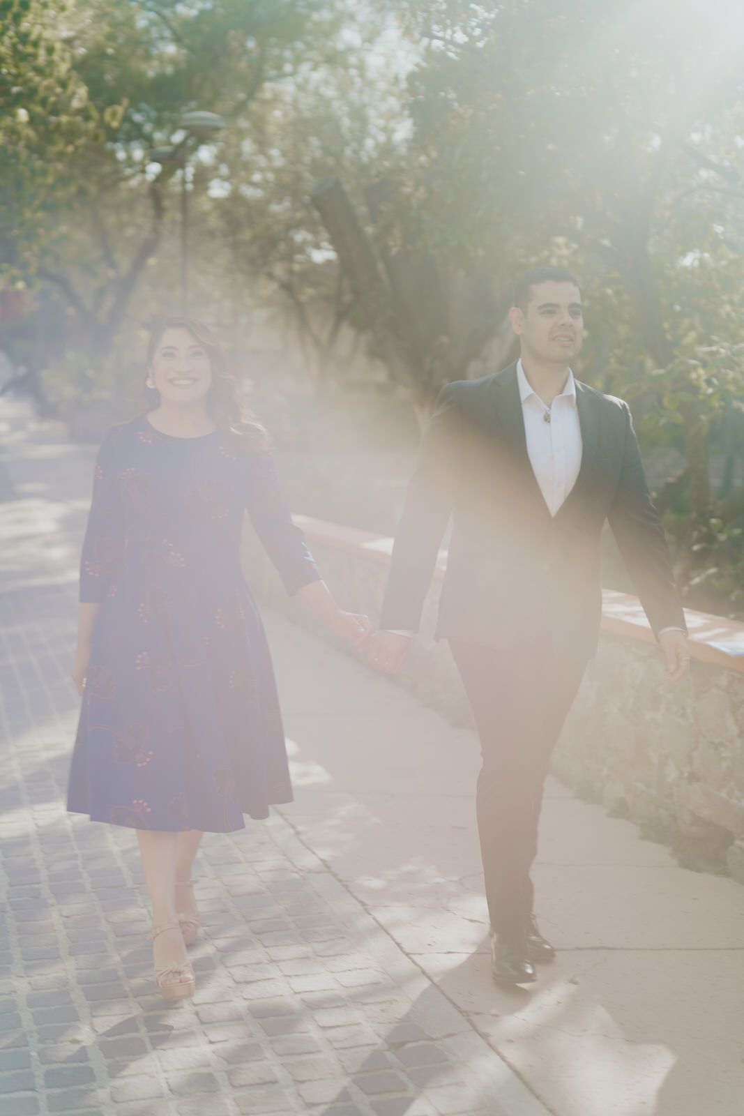 Sunlit pathway with couple walking together in formal attire.