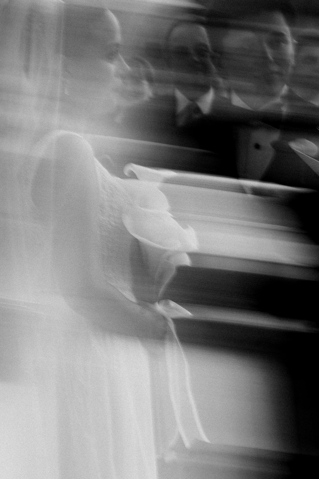 Blurred black and white photo of a bride in a white gown holding flowers at a wedding ceremony.