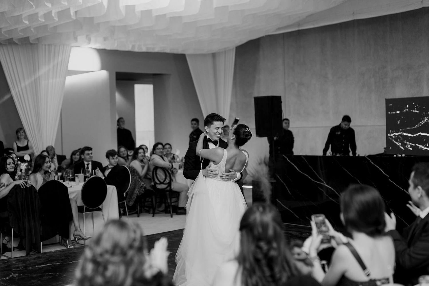 Bride and groom kiss during first dance at a wedding reception in black and white.
