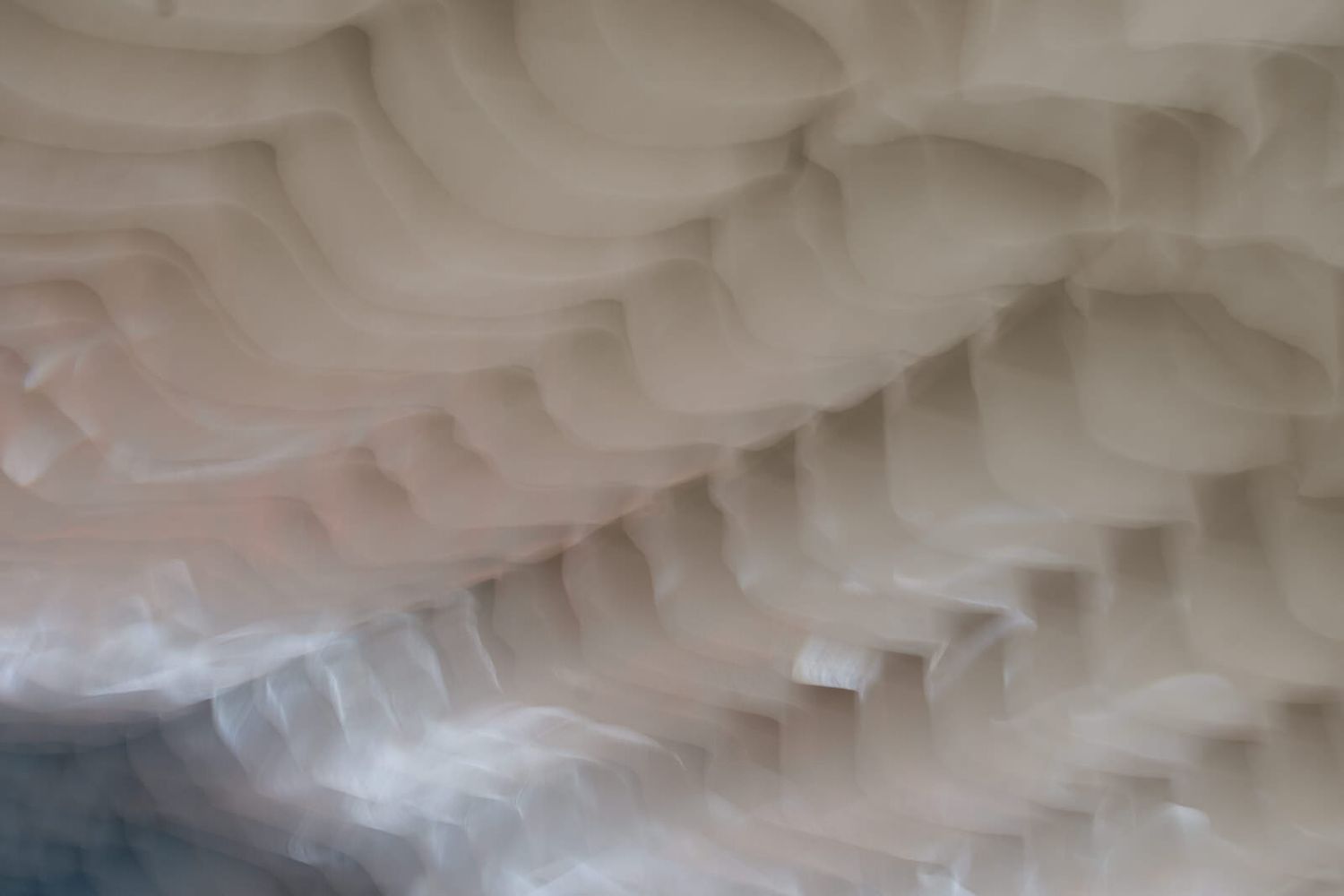 Abstract close-up of soft white and pink wavy textured layers resembling ice formations or fabric folds.