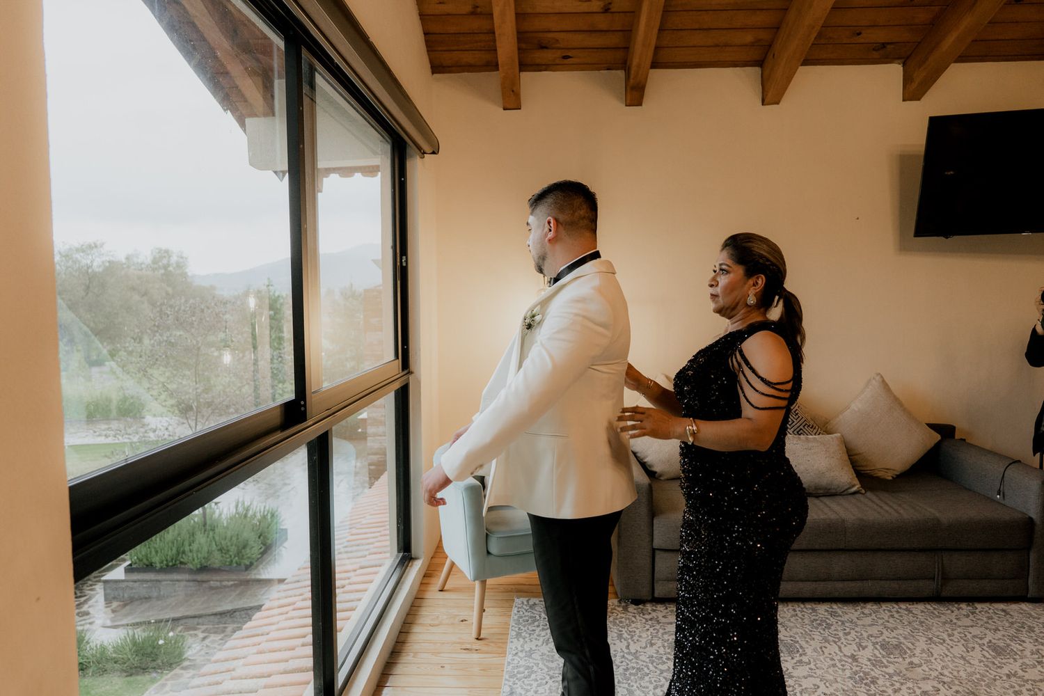 Wedding party members gather in a modern venue with exposed wooden beams and large windows.