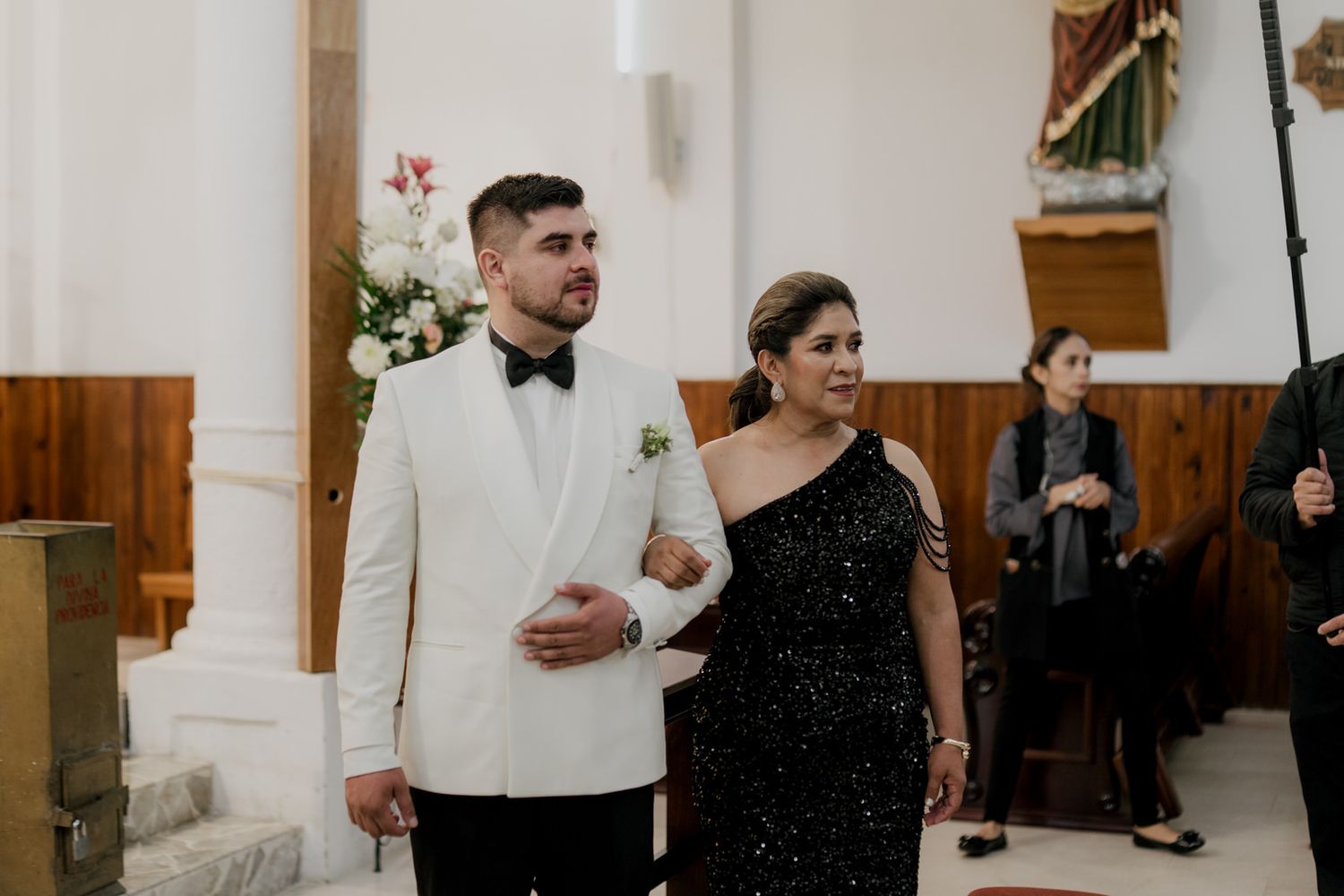 Wedding ceremony in progress inside traditional church with white walls and wooden details.