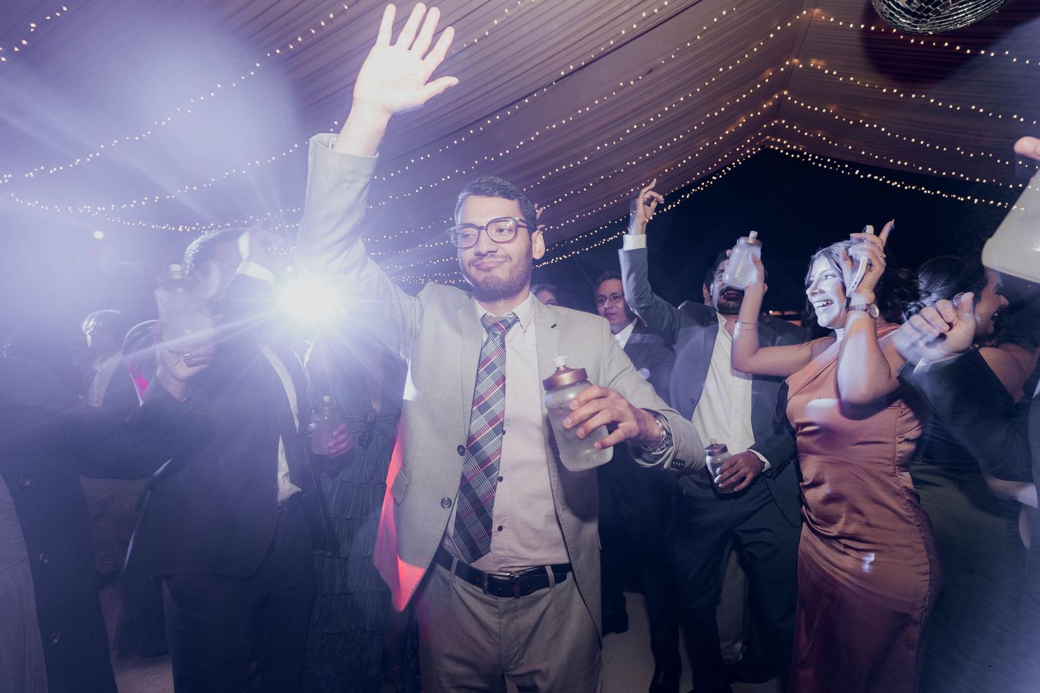 Party guests dancing under purple-tinted lighting at wedding reception.
