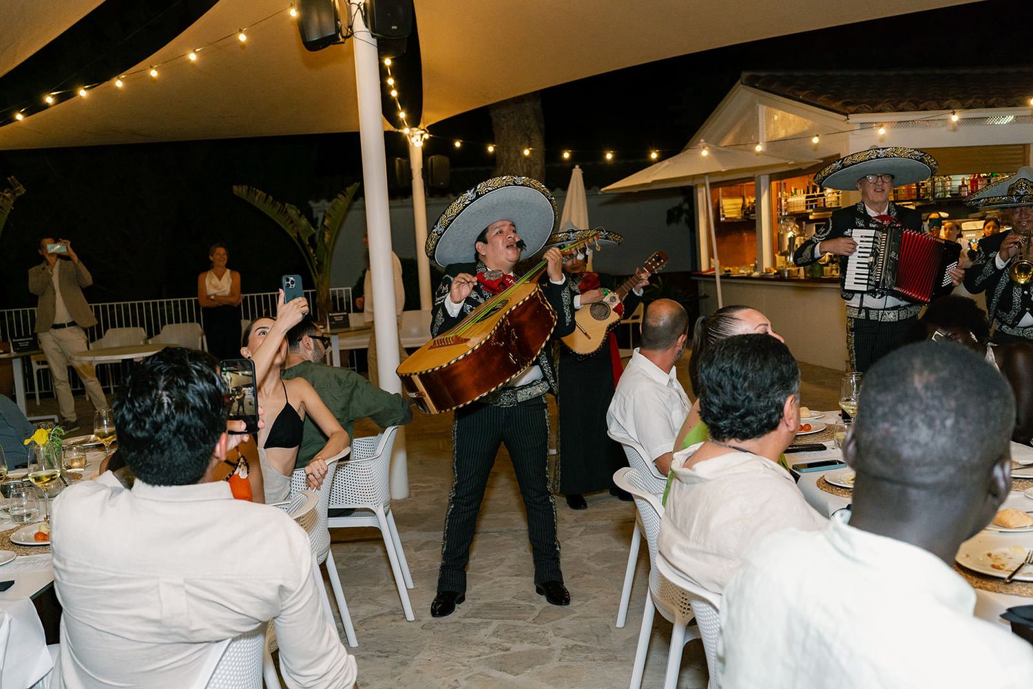 Reception hall filled with guests enjoying a celebration under white tent lighting.