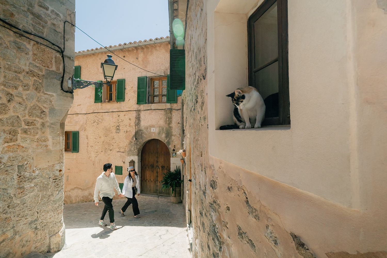Stone walkway with green shuttered windows and rustic architectural details in a Mediterranean village.