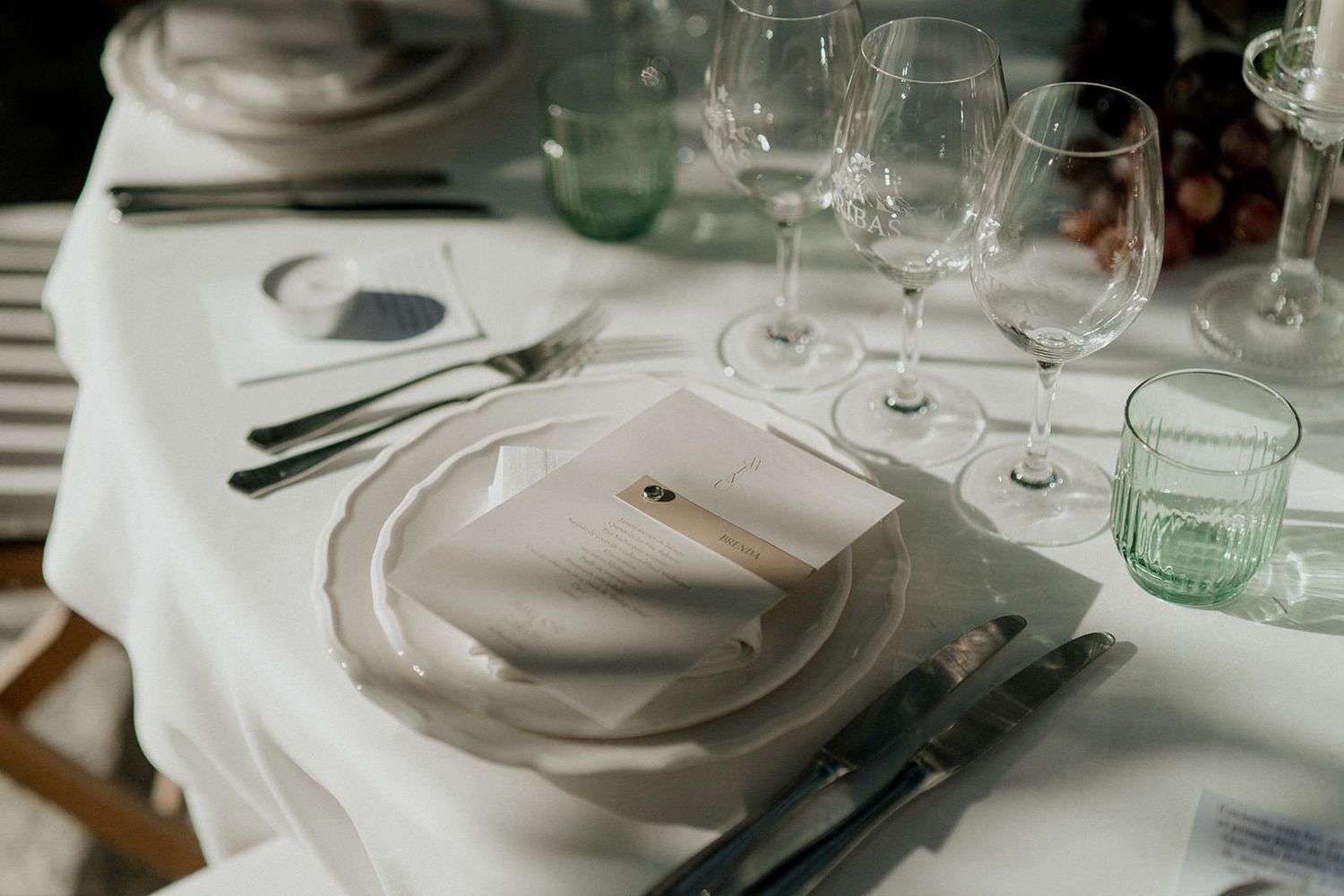 Elegant table settings with white linens and green glass vessels at a wedding reception.