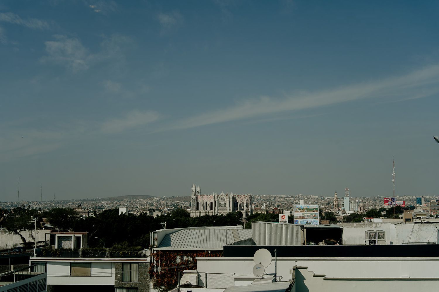 Panoramic cityscape view under a blue sky with scattered clouds showing urban rooftops and distant skyline.