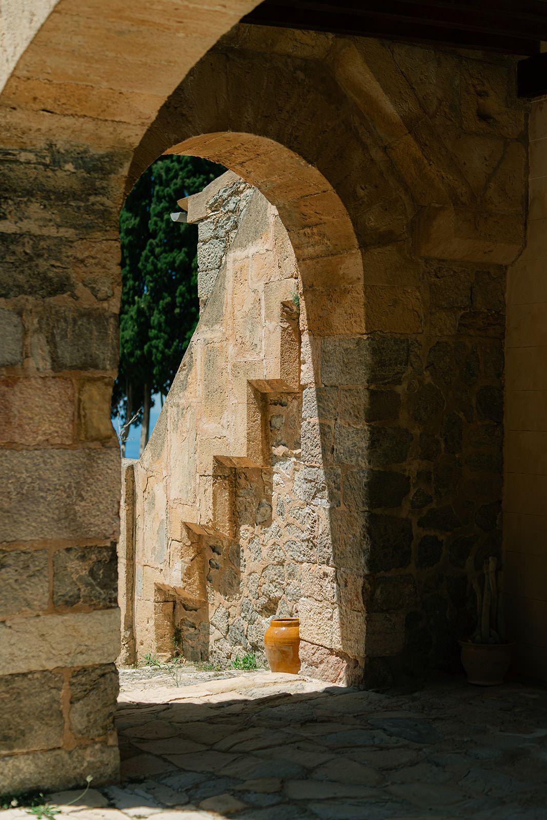 Stone archways in an ancient Mediterranean structure create a shadowy passageway with sunlit openings.