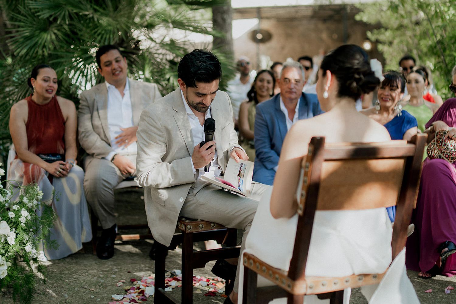 Wedding guests gather outdoors at a rustic celebration with natural greenery and trees in the background.
