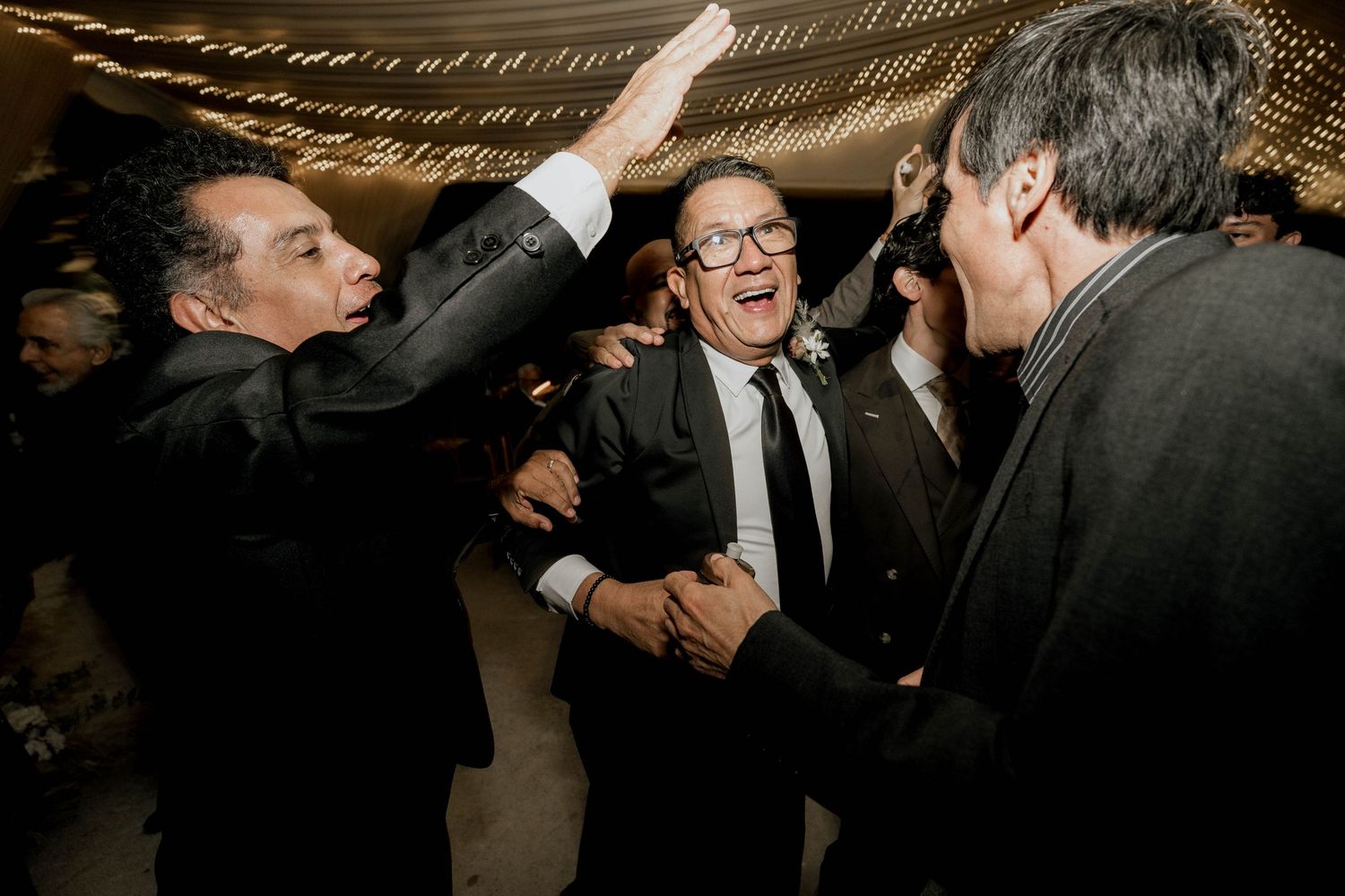 Guests celebrating on the dance floor under string lights at an elegant wedding reception.