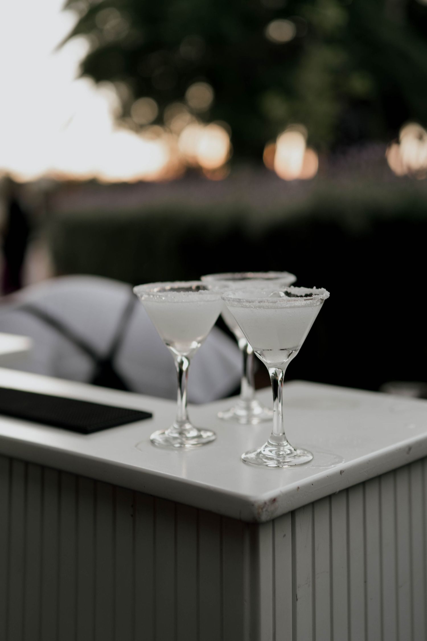 Elegant martini glasses arranged on a gray bar counter at dusk.