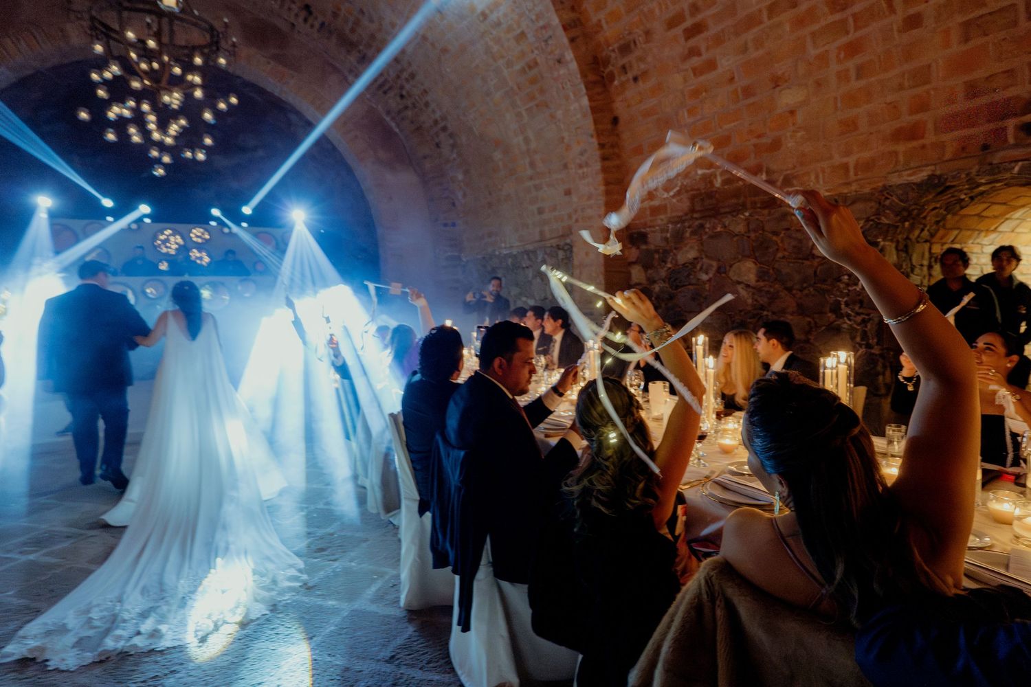 Wedding celebration in brick tunnel venue with dramatic lighting and dancing silhouettes.