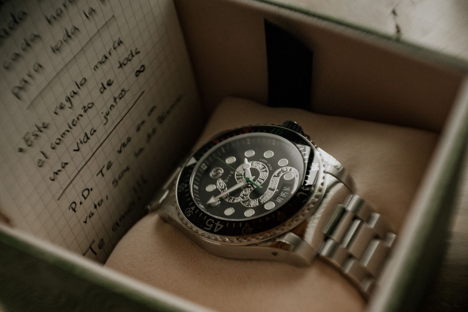 A luxury wristwatch with dark face and metal band rests in a box.