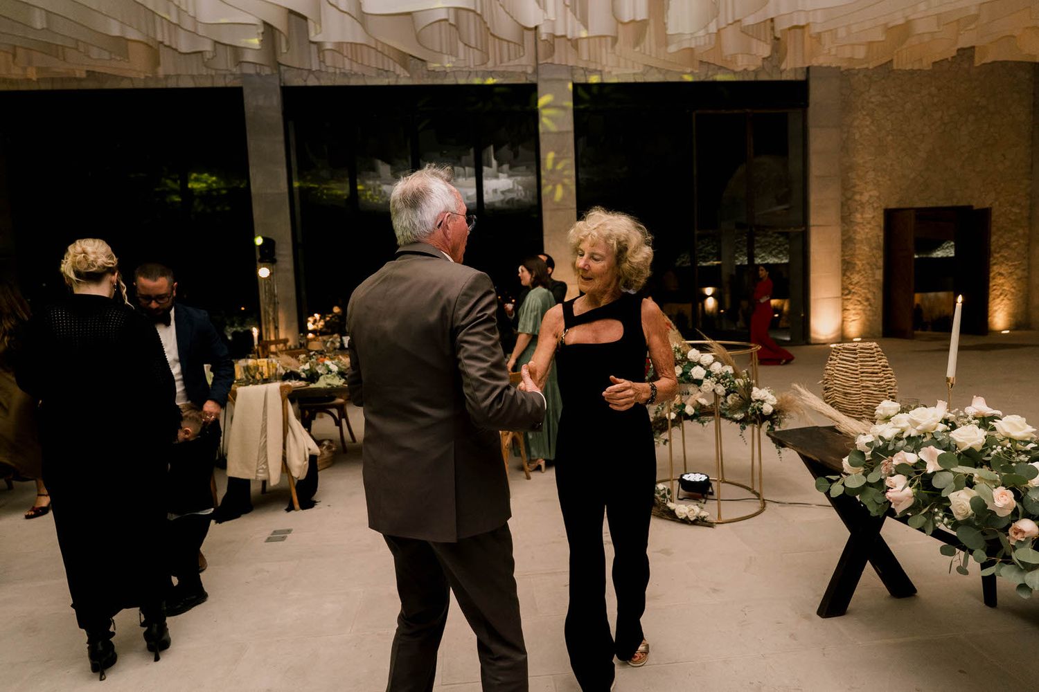 Elegant floral arrangements decorate a wedding reception venue with guests mingling on the dance floor.