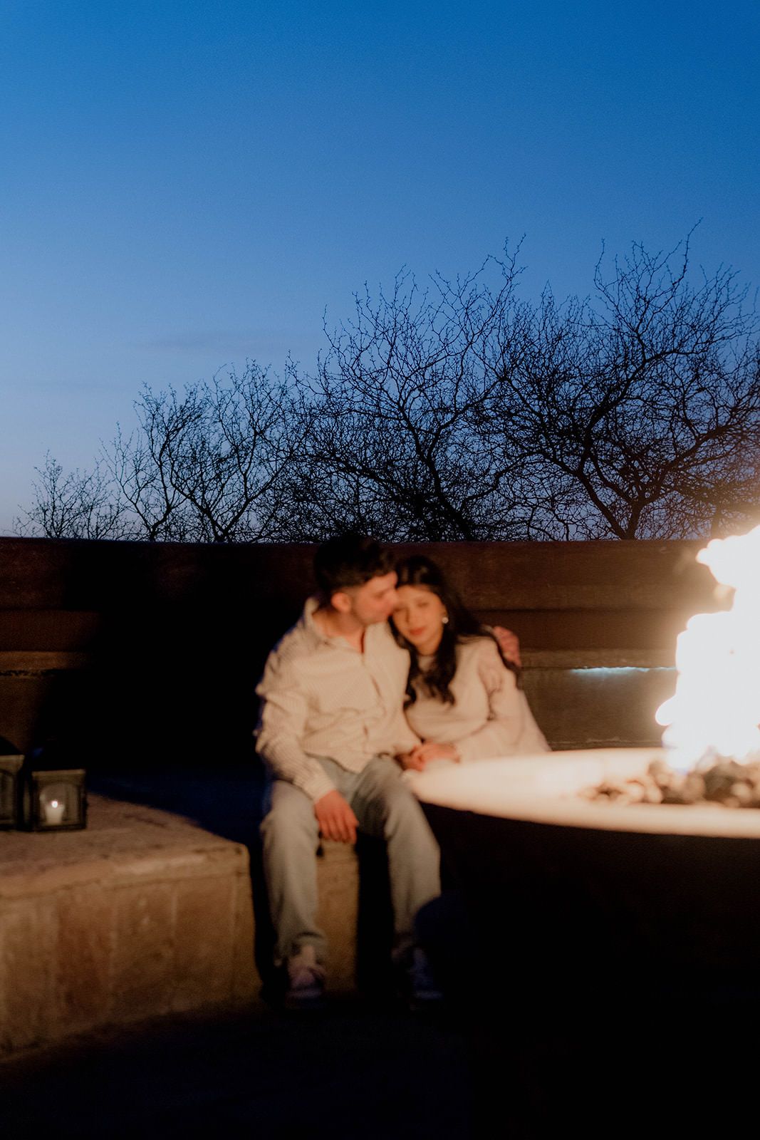 Intimate evening moment by fire pit under bare winter trees and blue sky.