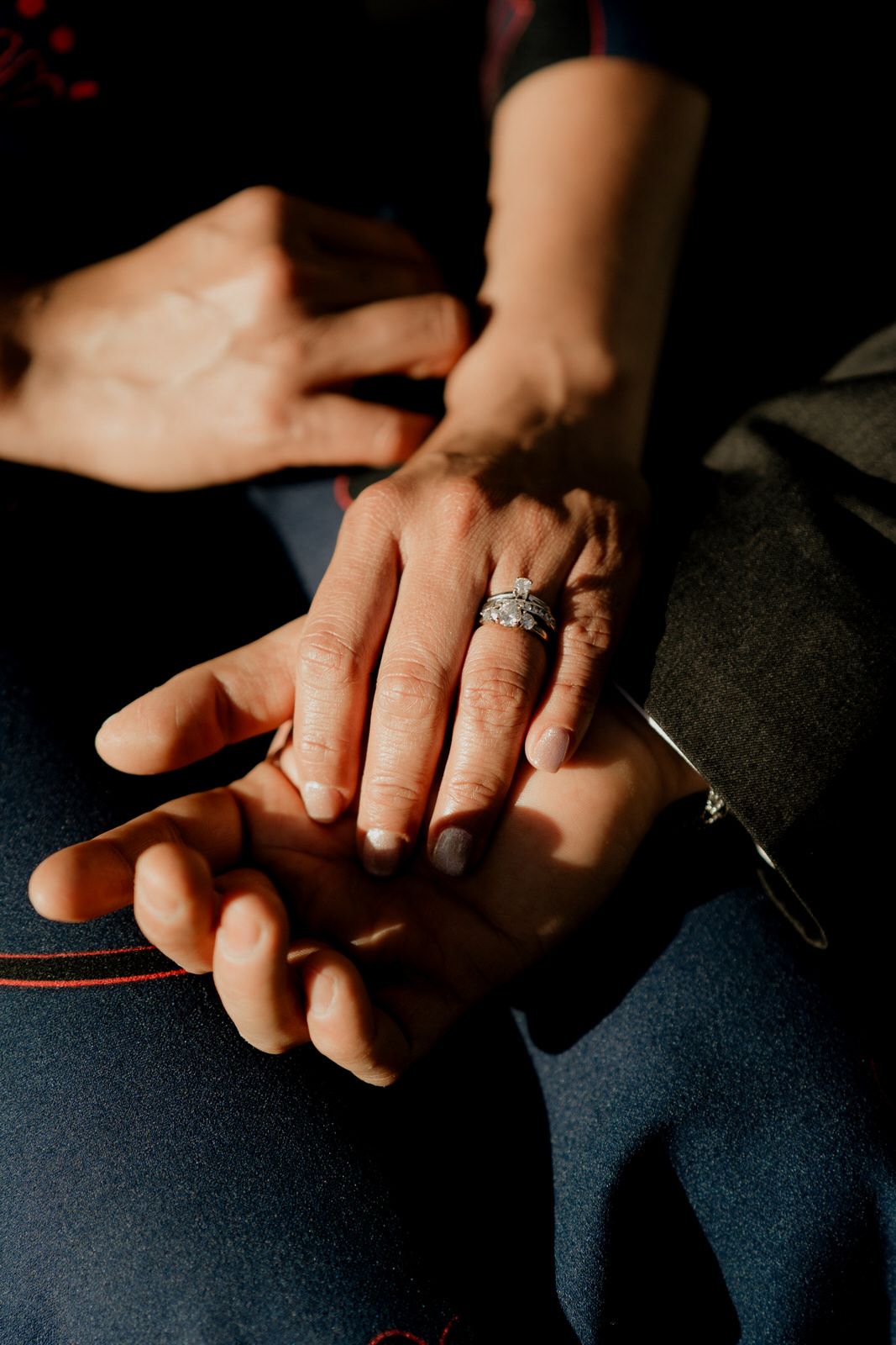 Close-up of hands clasped together showing engagement ring in dramatic lighting.