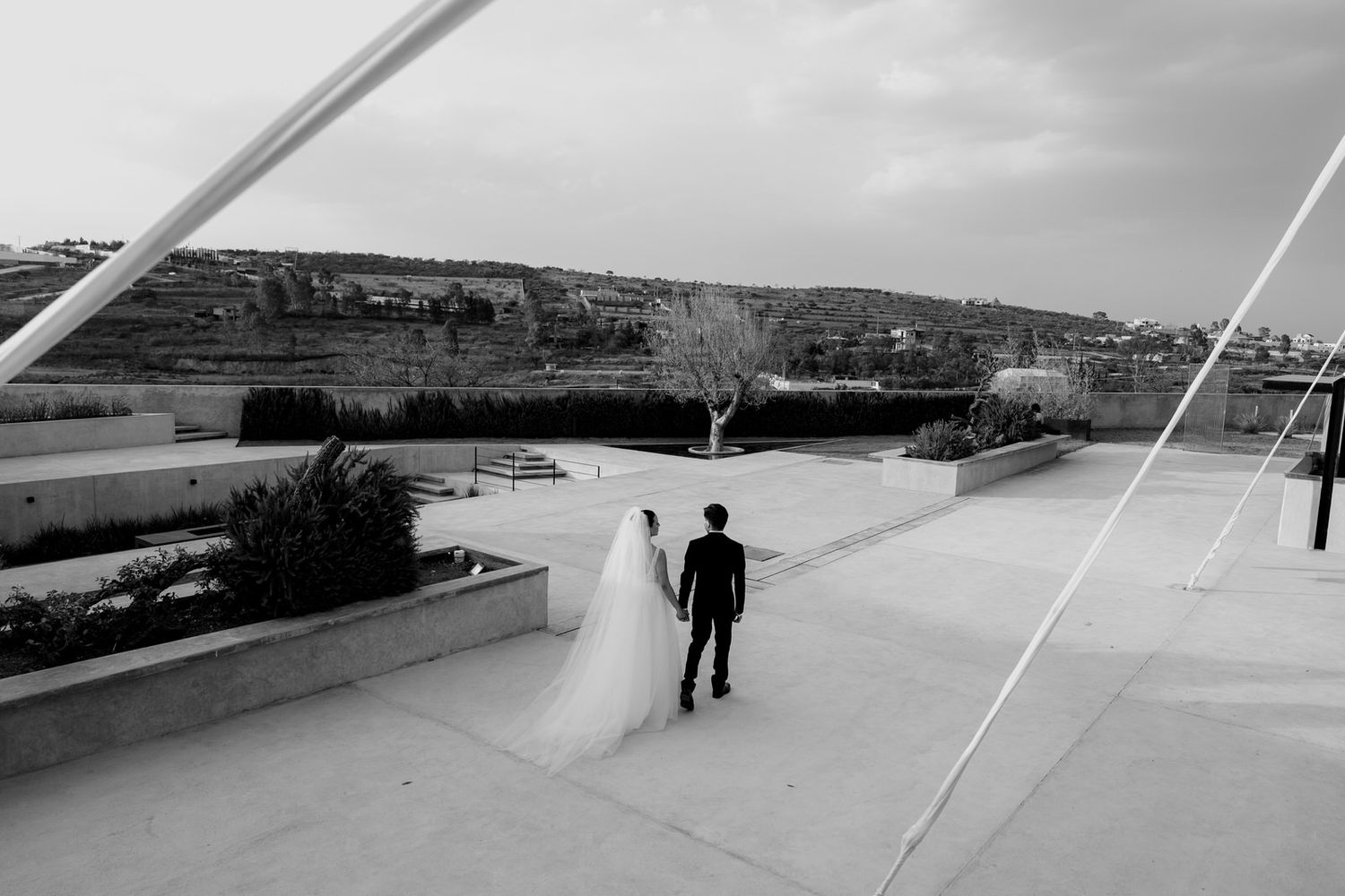 Black and white photo of bride and groom walking hand in hand on rooftop.