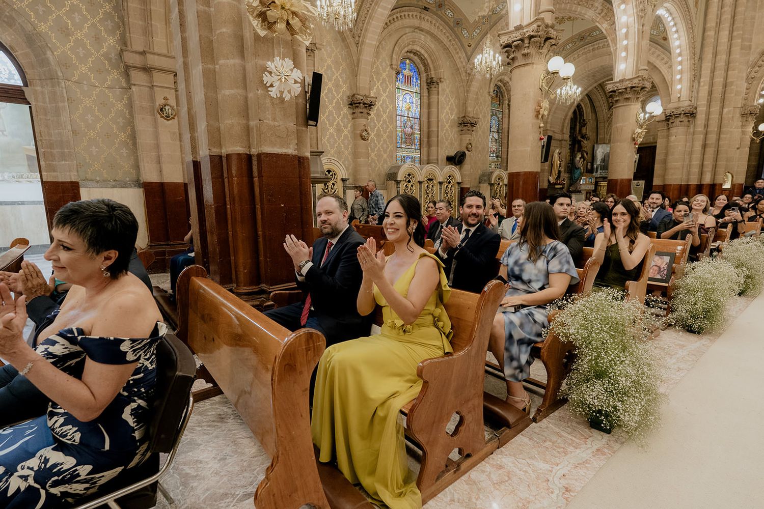 Wedding guests applaud in ornate church with wooden pews during beautiful ceremony.