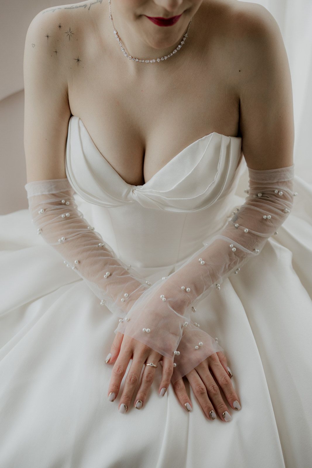 Elegant bridal details featuring sheer pearl-adorned gloves and a sweetheart neckline gown.
