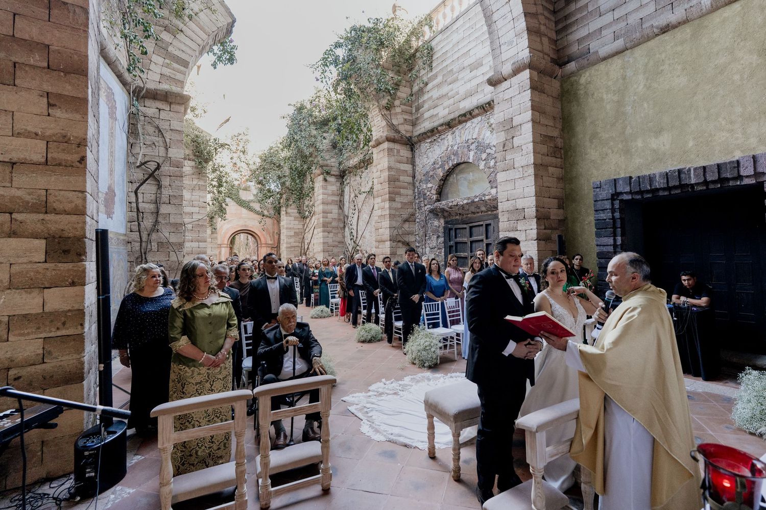 Wedding ceremony taking place in a historic stone corridor with natural light streaming through.