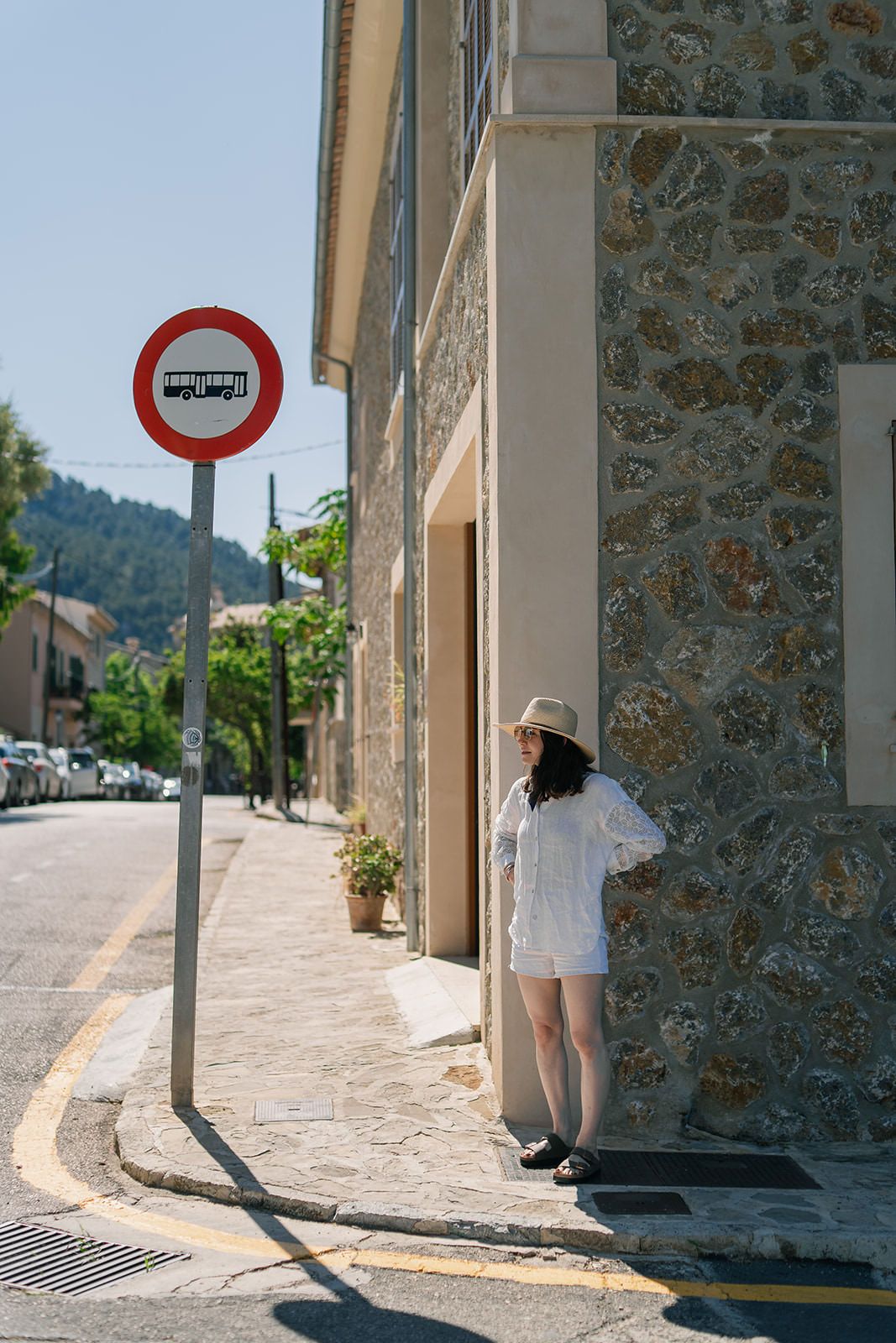 Person in white clothing walking down a narrow cobblestone street with stone buildings and a traffic sign.