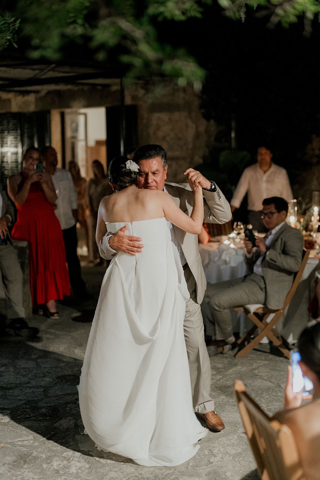Romantic couple dancing together at a dimly lit wedding reception with guests watching in the background.