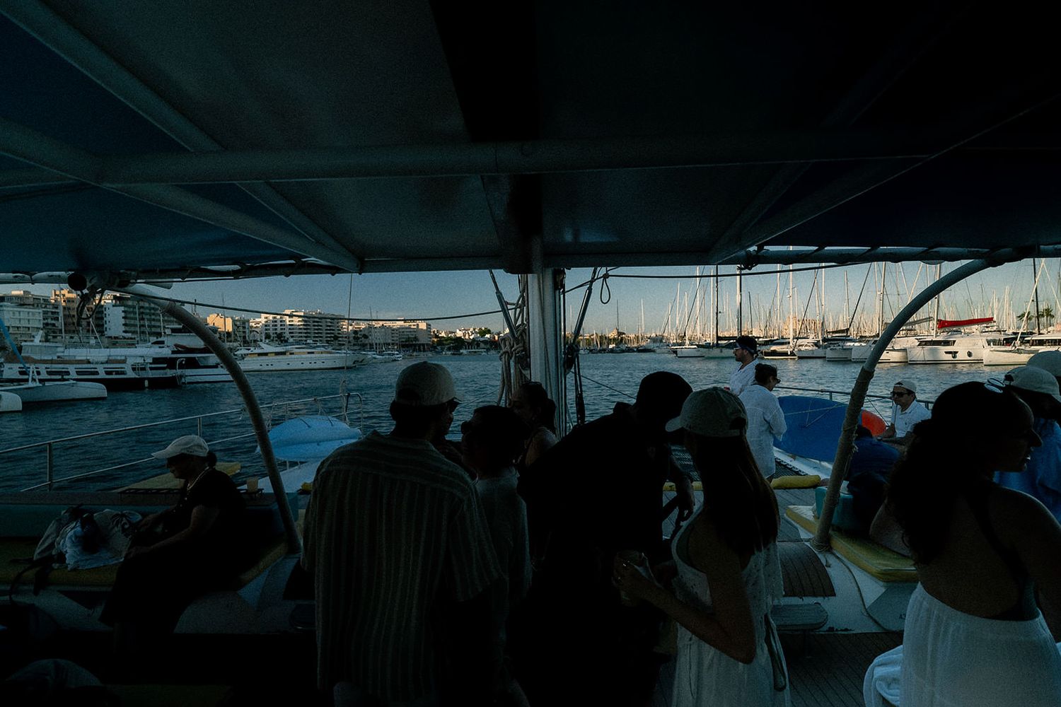 Silhouetted passengers on a boat tour view the marina and harbor at dusk through the vessel's windows.