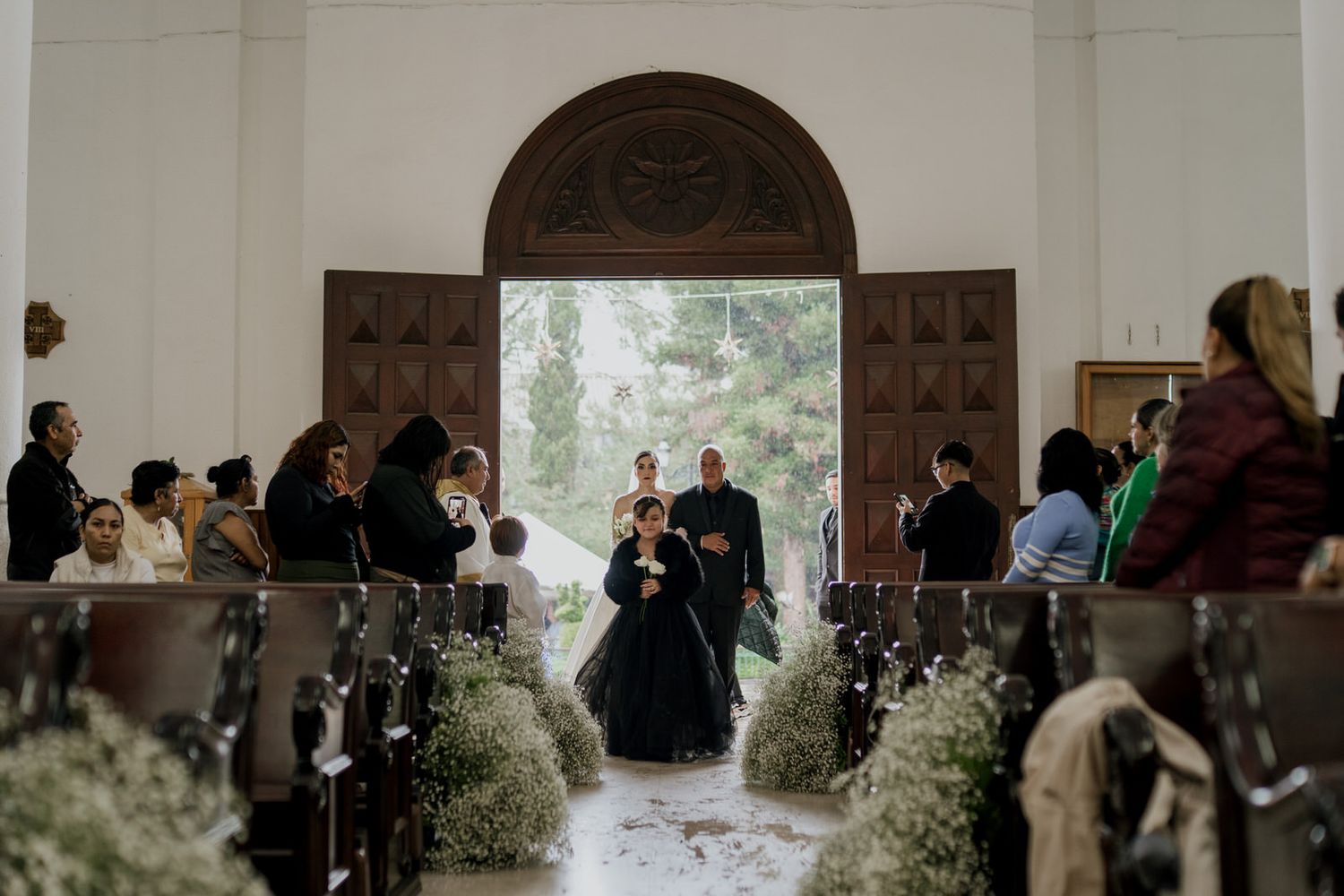 Wedding guests seated in wooden church pews with baby's breath floral decorations along the aisle.