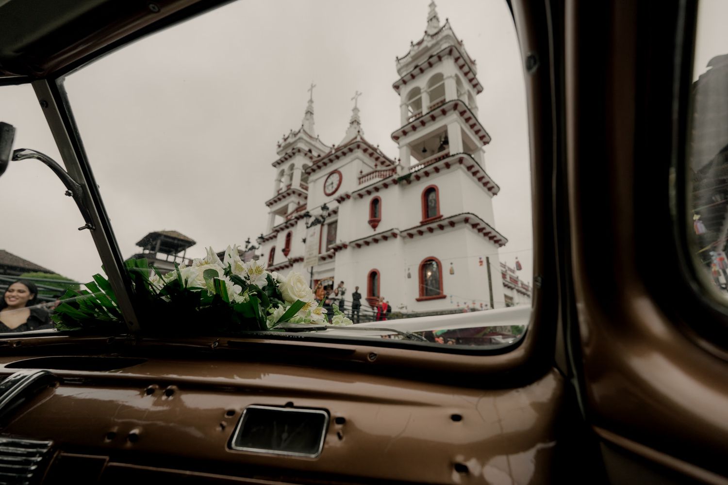 View of ornate white church towers with twin spires through vintage car windshield.
