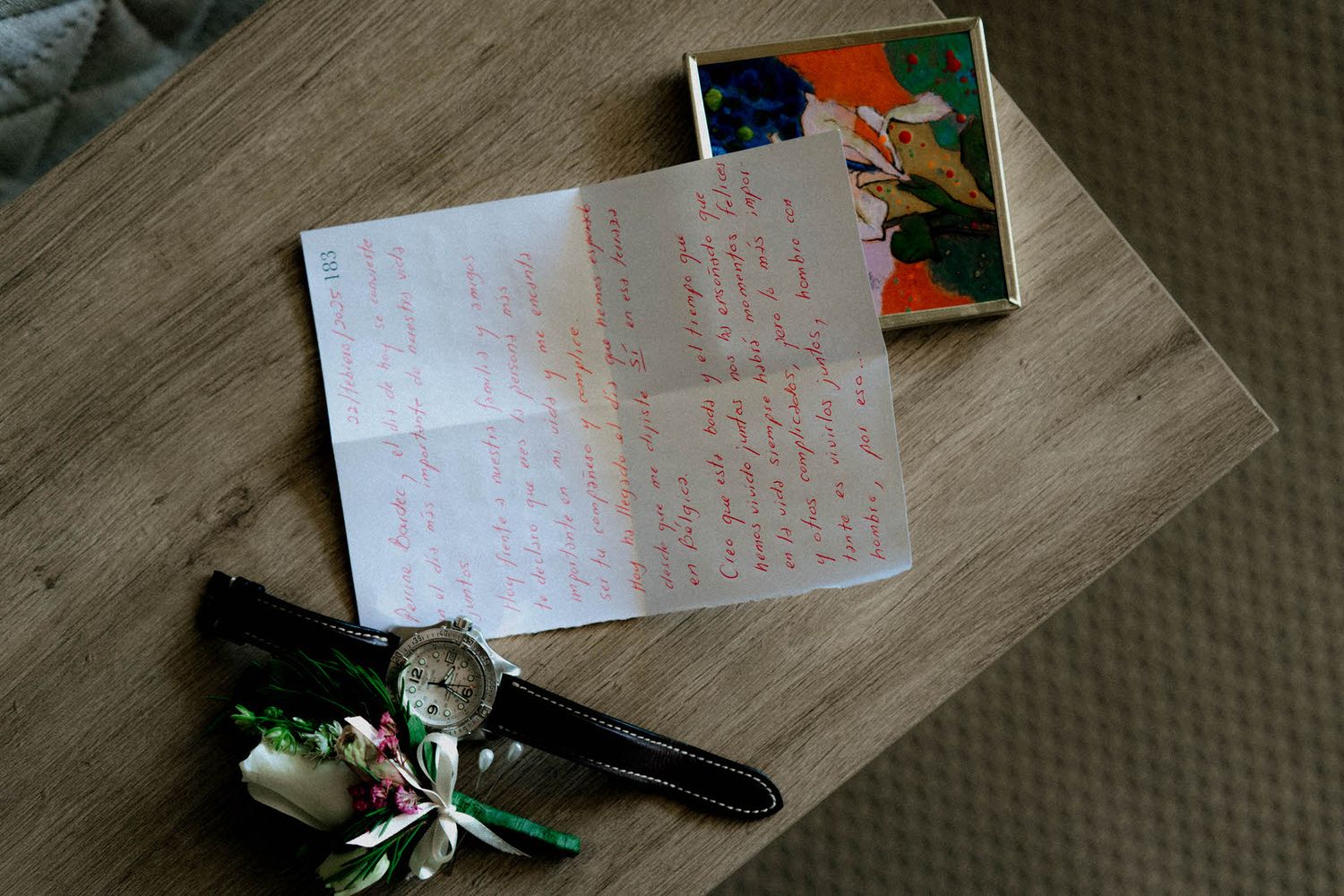 A handwritten note lies on a wooden surface next to a boutonniere and decorative elements.