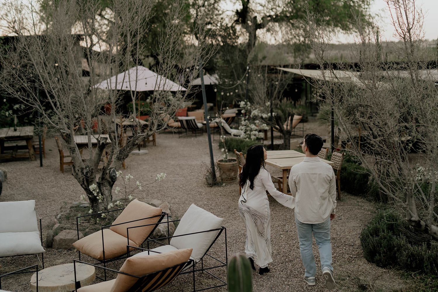 Two people walking together on outdoor path with desert vegetation in background.
