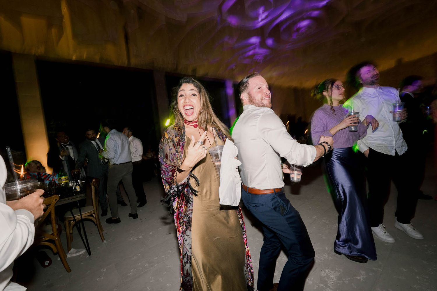 Party guests dancing and celebrating under purple mood lighting.
