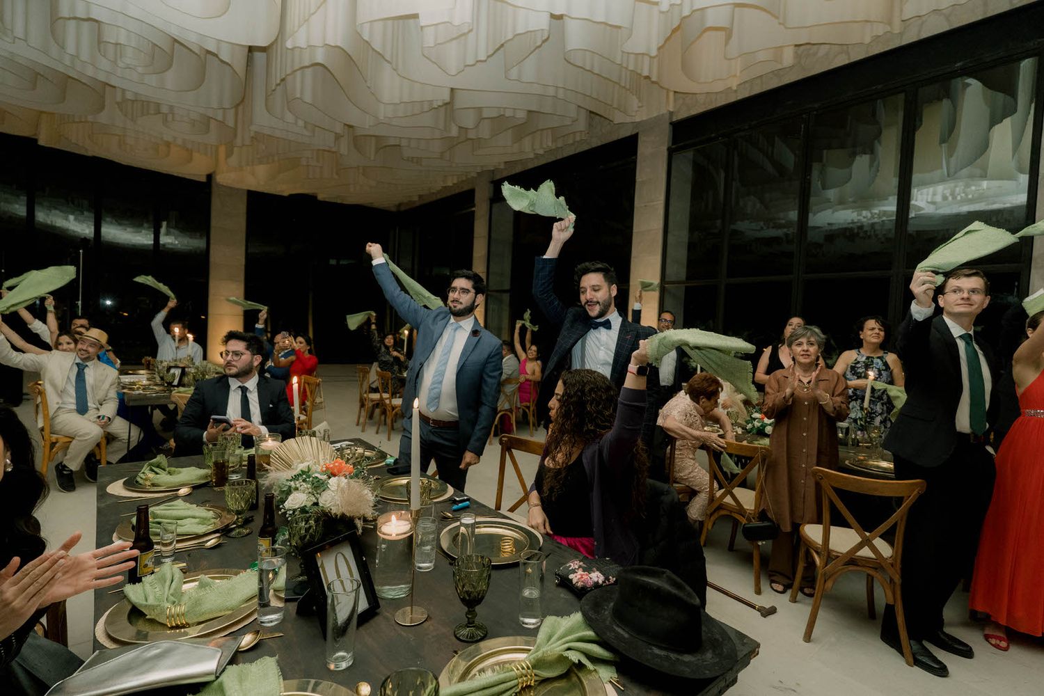 Wedding guests seated in an elegant reception venue with stone walls and draped fabric ceiling.