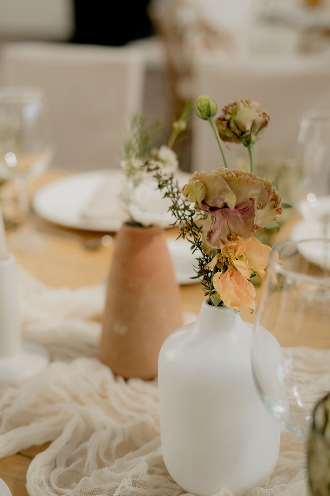 Elegant wedding table centerpiece with white and terracotta vases holding peach and white flowers.