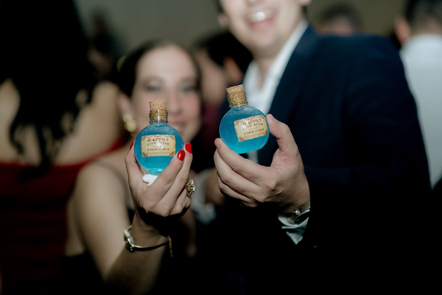 Two people holding turquoise blue decorative bottles with cork stoppers at a party.