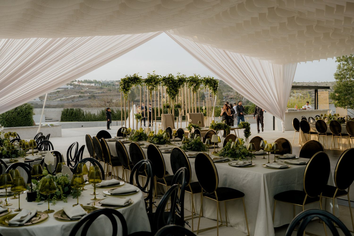 Elegant outdoor wedding reception under white draped tent with black chairs and green centerpieces.