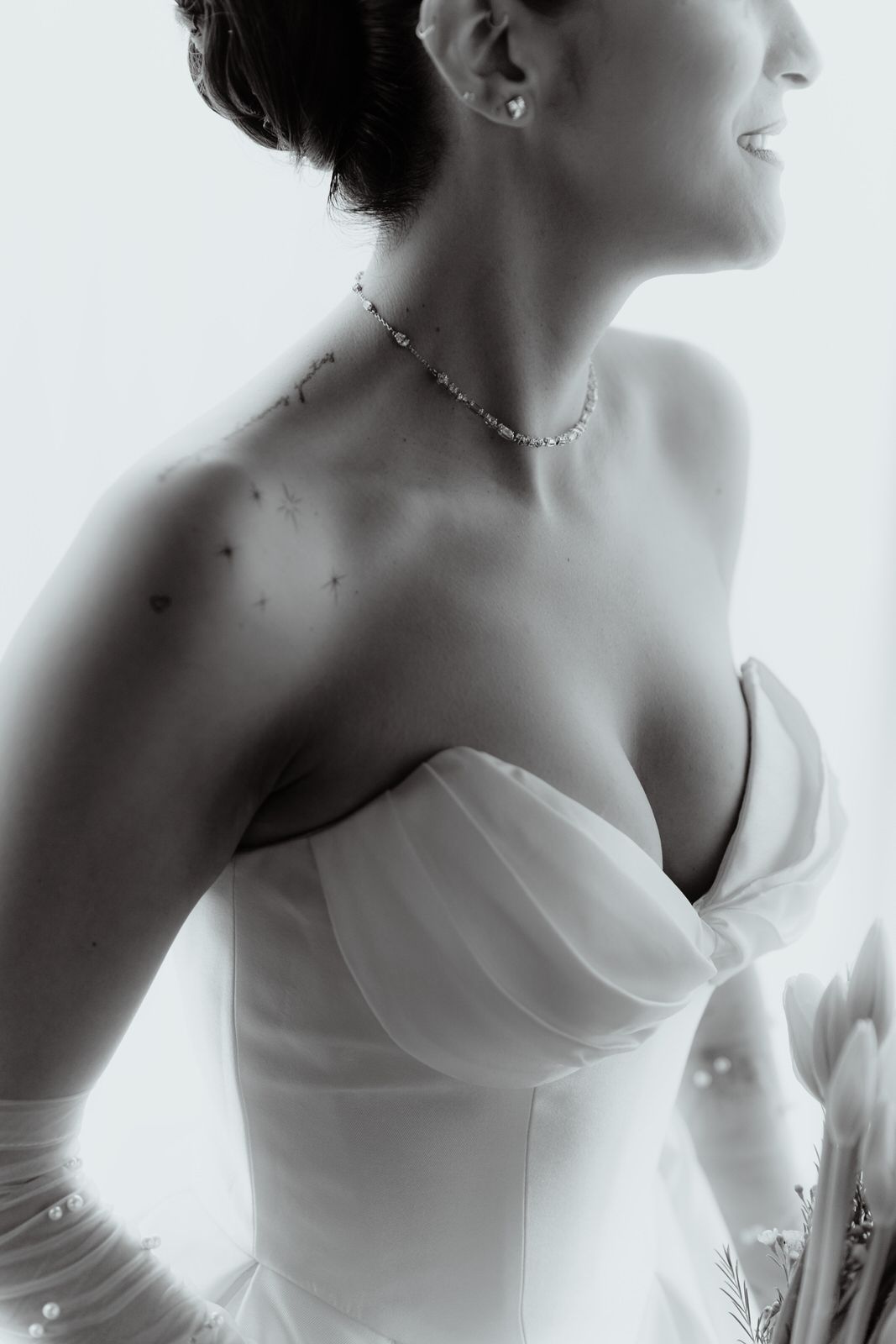 Artistic black and white portrait showing delicate jewelry and strapless wedding dress details.