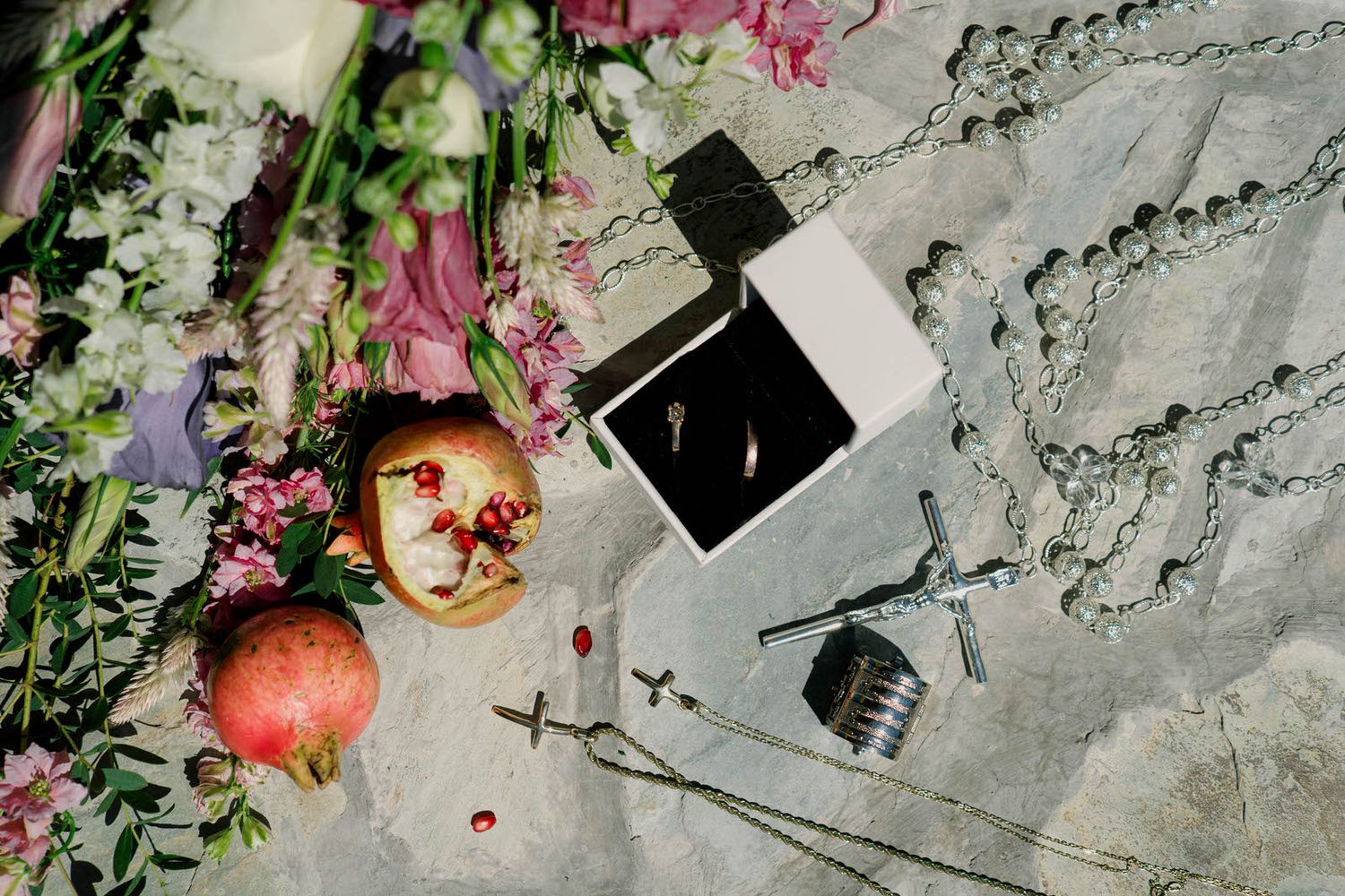Artistic flatlay with pomegranate, flowers and polaroid photo on textured surface.