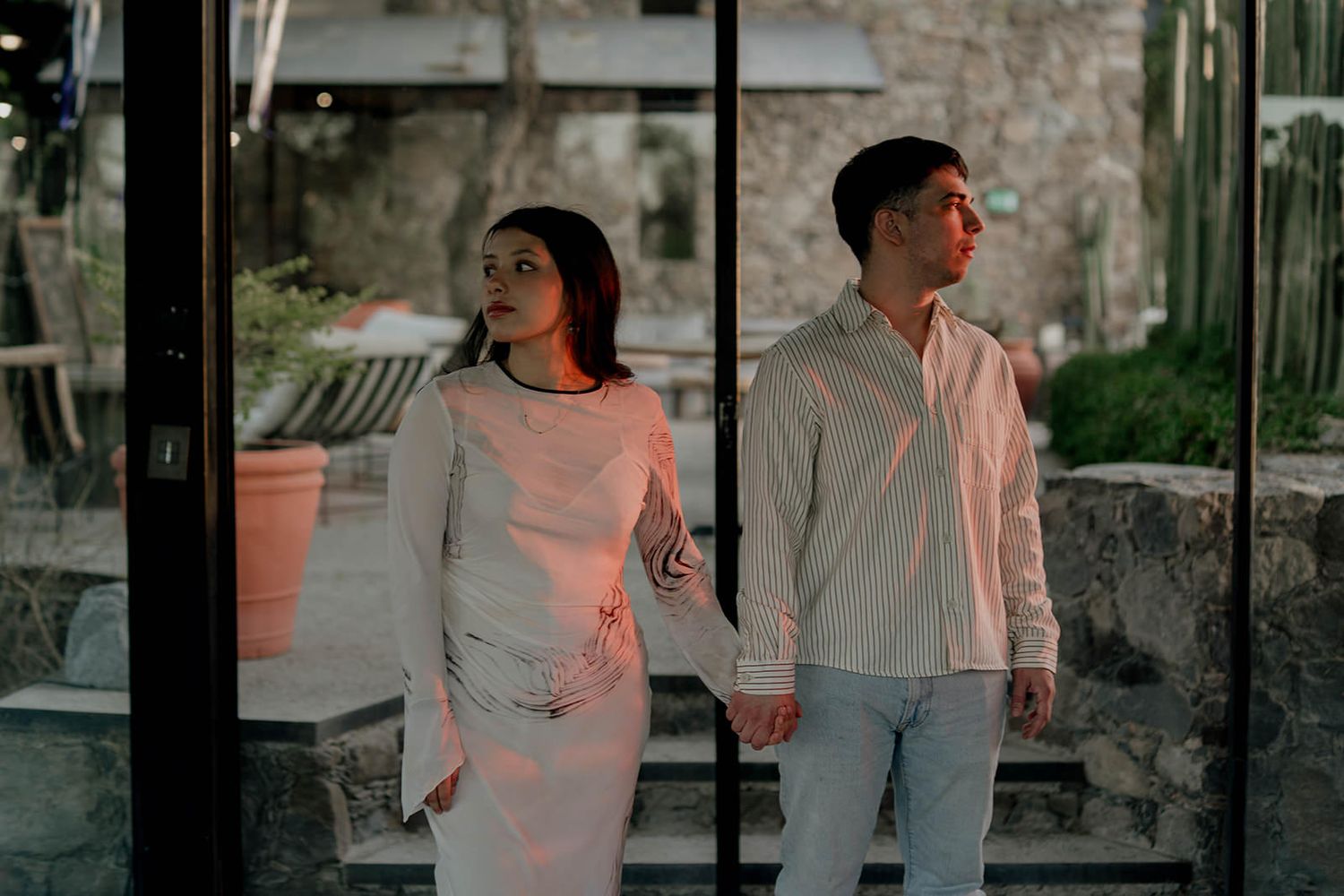 Couple in light colored outfits posing against stone wall background.