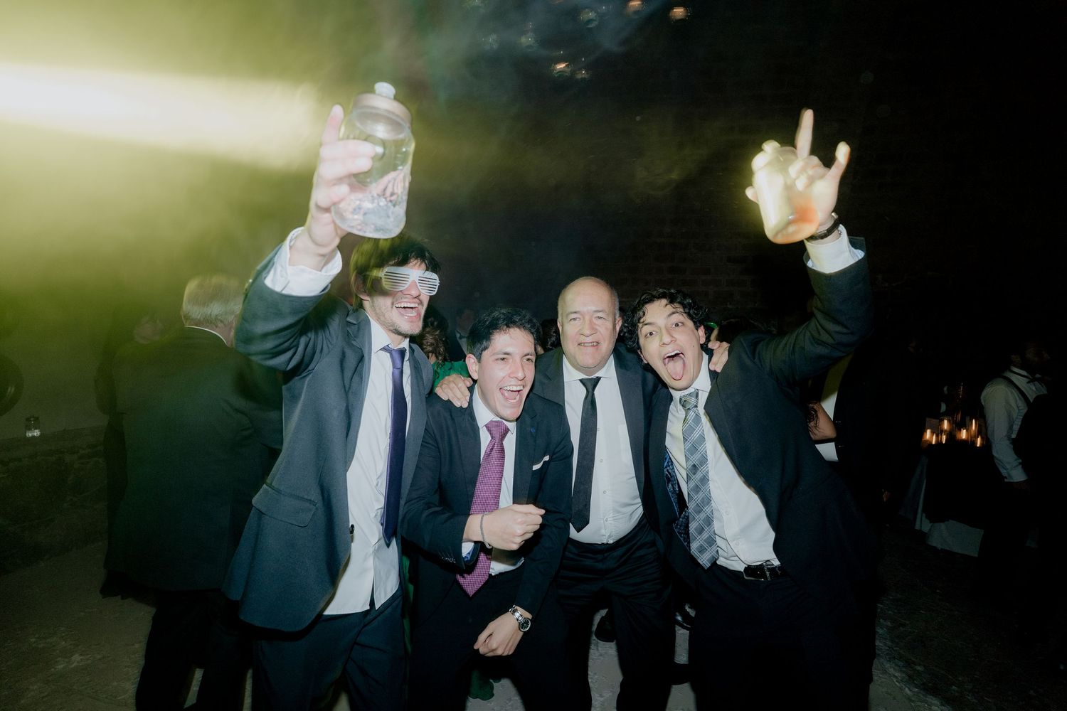 Wedding celebration with guests dancing under moody lighting and smoke effects.