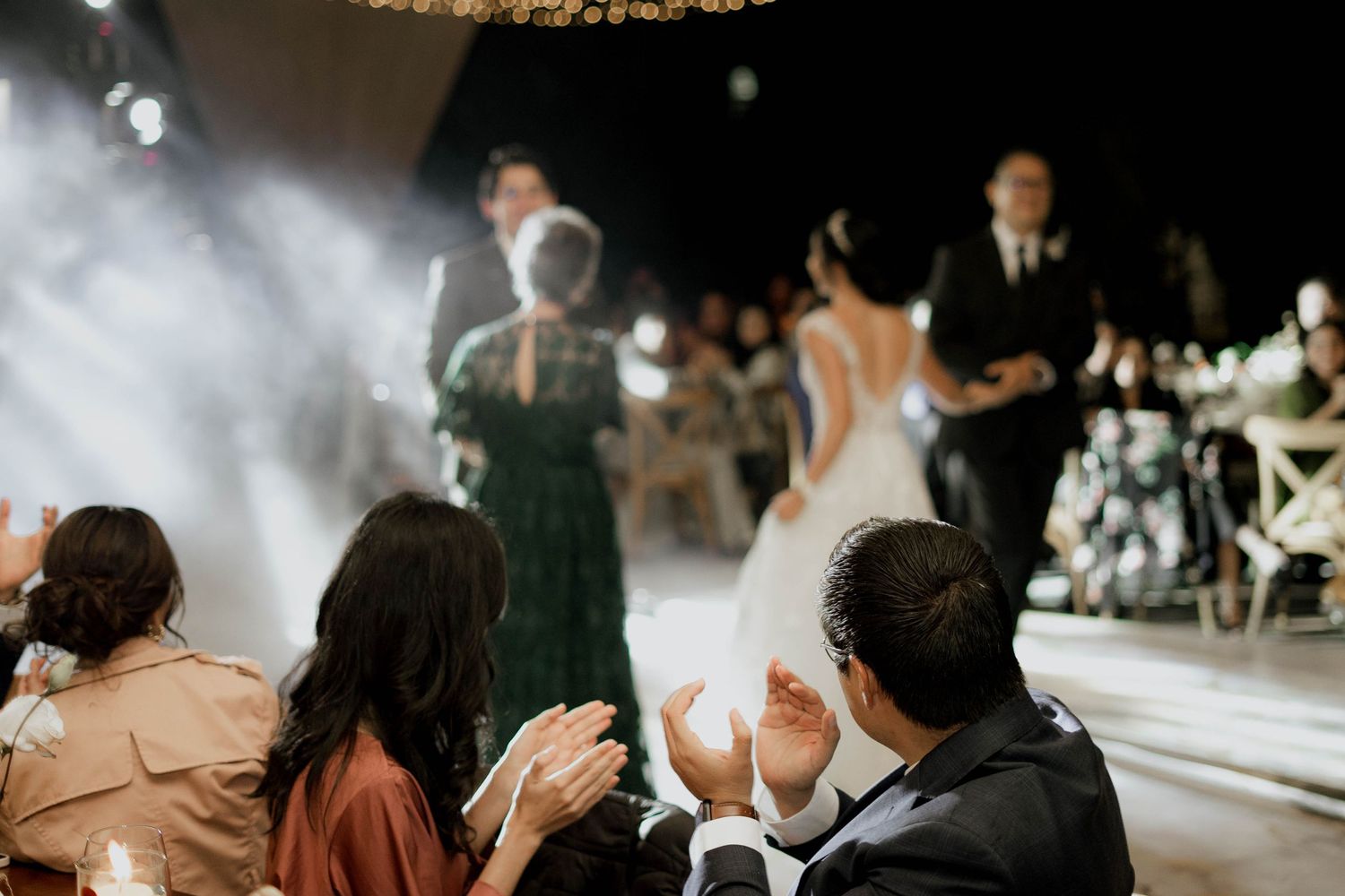 Wedding guests dance under twinkling lights and fabric draping at an evening reception.