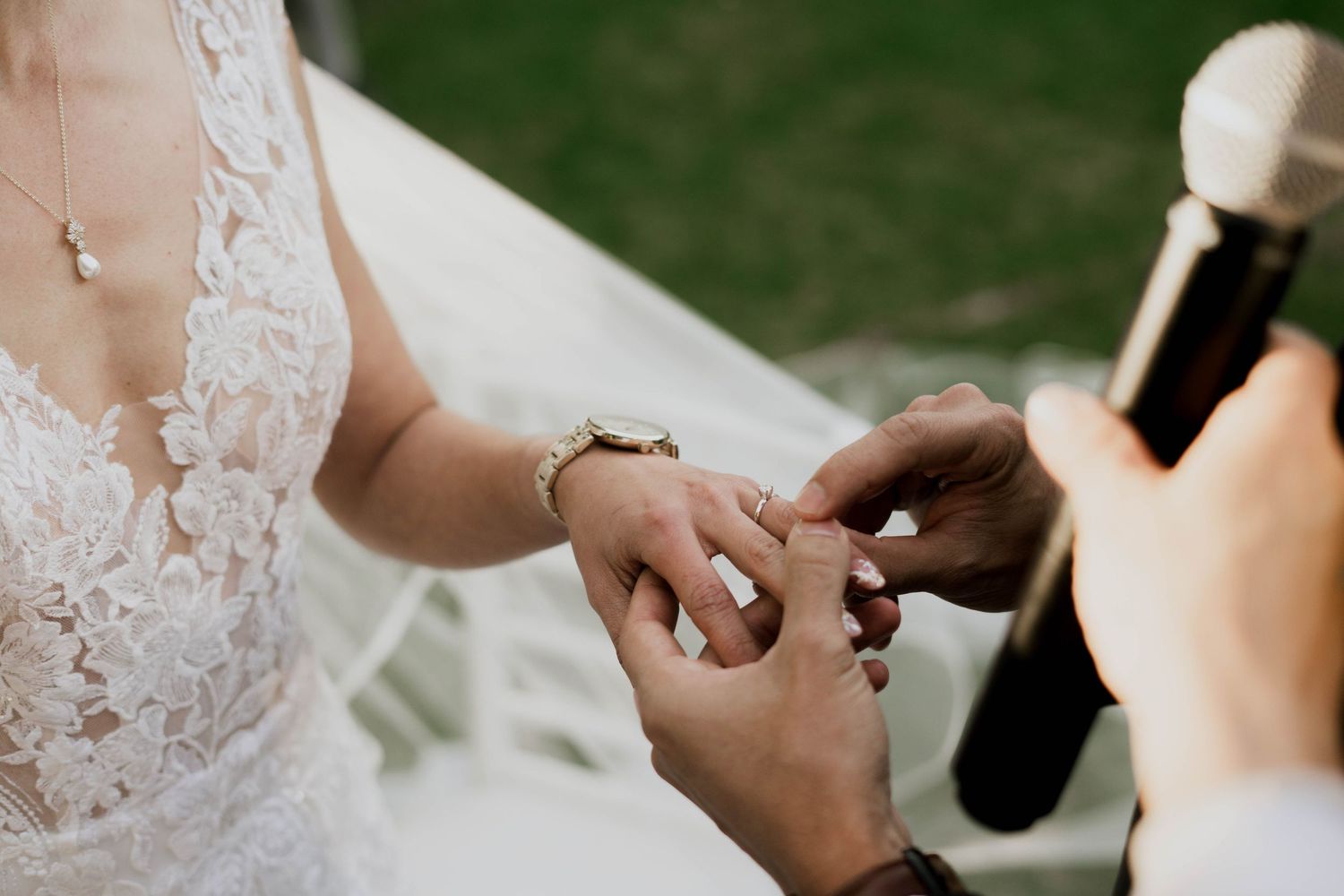 Hands exchanging rings during outdoor wedding ceremony.