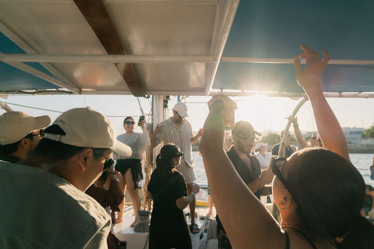 People dancing and celebrating at a sunset party on a boat with arms raised in the air.