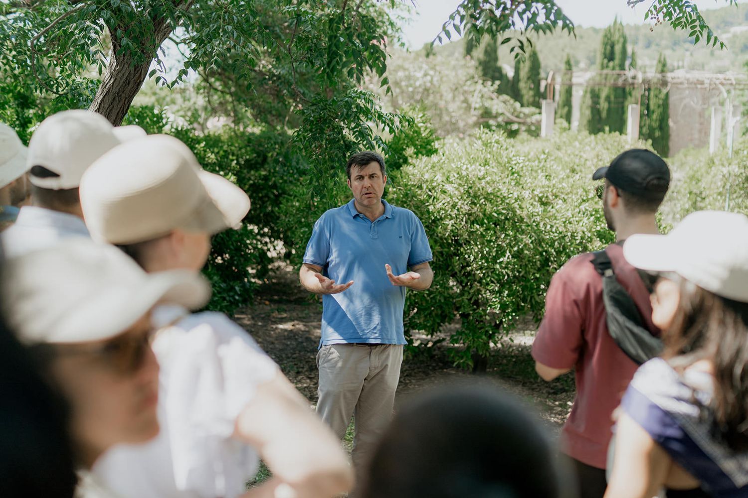 People gather outdoors in a garden setting during a social event on a sunny day.