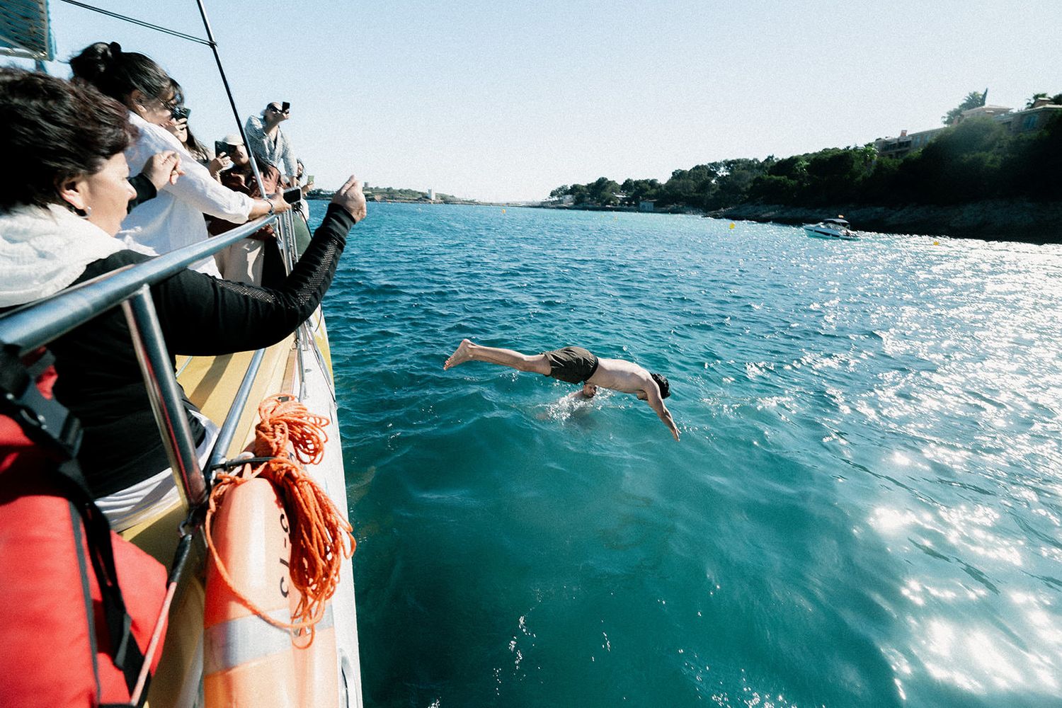 Group swimming in crystal clear turquoise waters next to a sailing boat.