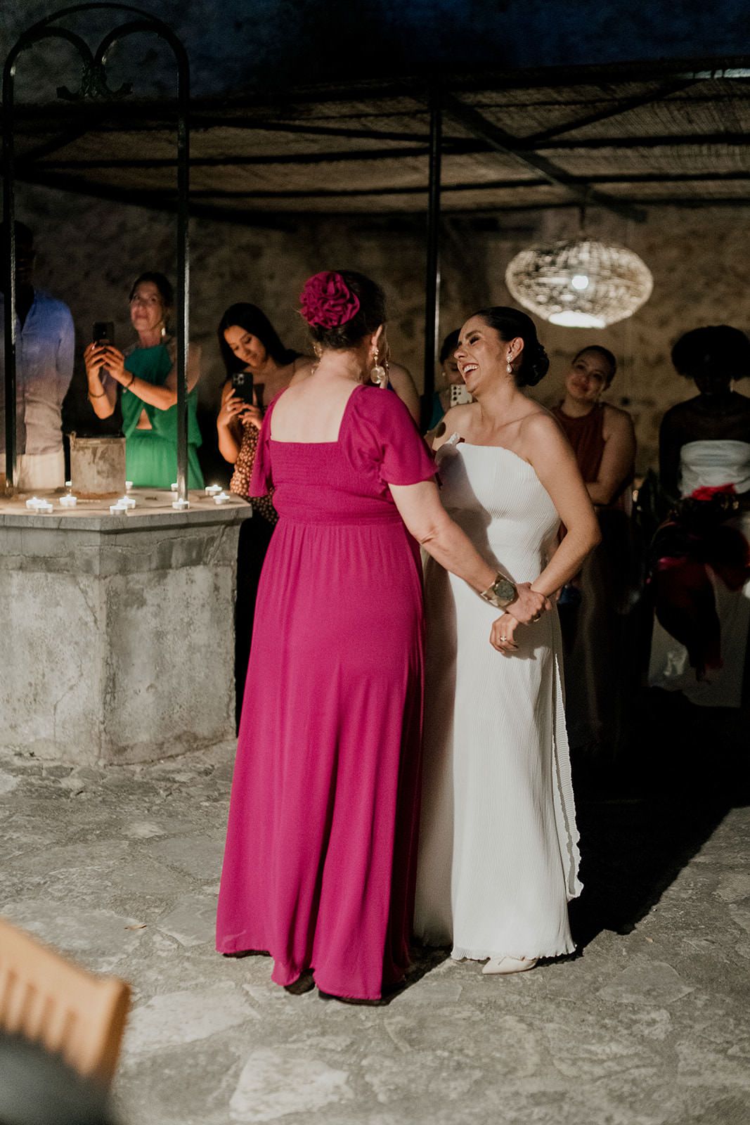 Guests in formal attire dancing and celebrating at an indoor wedding reception with stone walls.