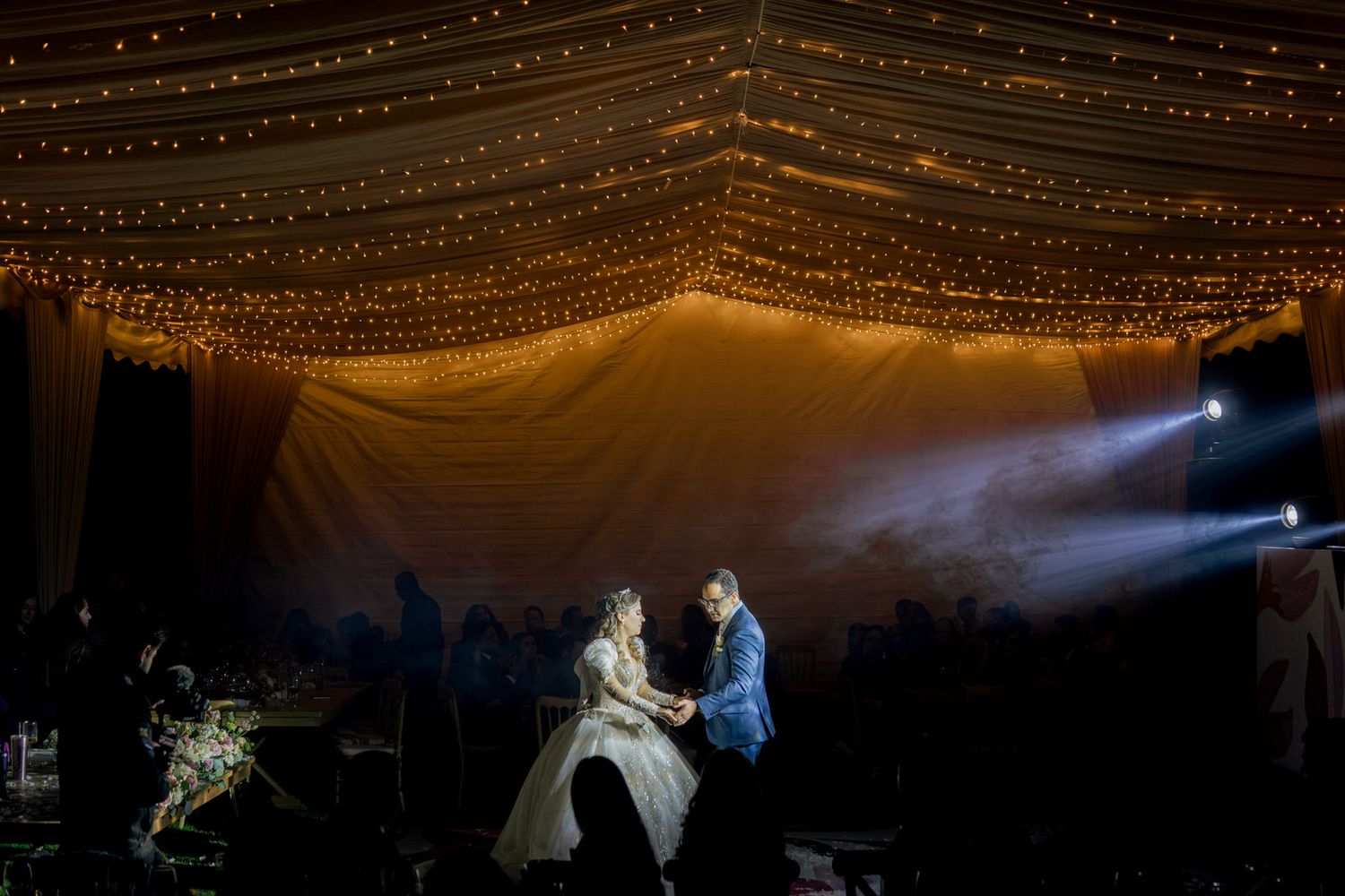Romantic dance scene under canopy of string lights with dramatic stage lighting.